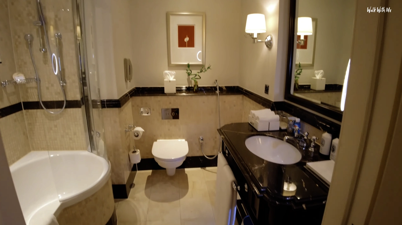 The Langham London — marble bathroom with bath, shower and dark vanity
