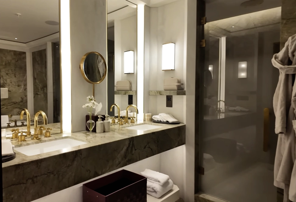 The Chancery Rosewood — double vanity marble bathroom with gold fixtures and glass shower